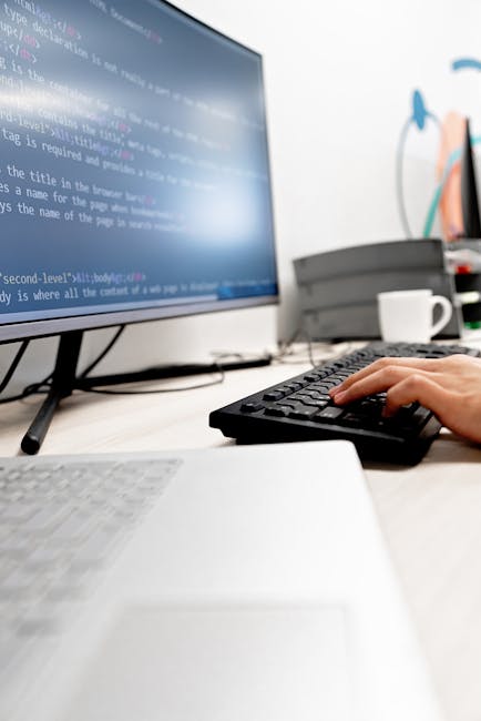 A close-up view of a silver laptop on a desk displaying a software development environment with lines of code on the left side of the screen and a large digital calculator interface with orange button